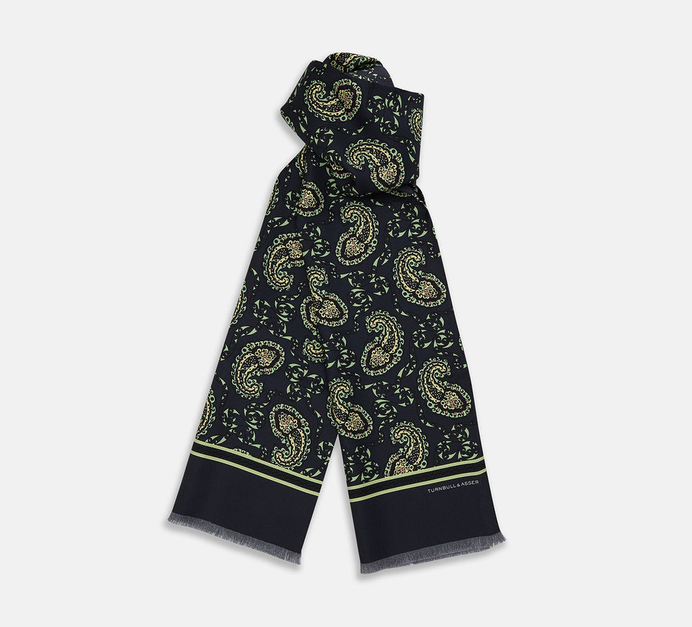 The Navy Paisley Silk Lawton Scarf by Turnbull & Asser features light green and cream paisley, a thin green stripe near the ends, short fringes on the edge, and is expertly crafted at a renowned UK silk mill.