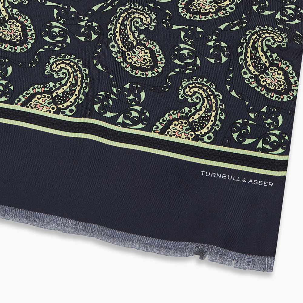 The Navy Paisley Silk Lawton Scarf by Turnbull & Asser features light green and cream paisley, a thin green stripe near the ends, short fringes on the edge, and is expertly crafted at a renowned UK silk mill.