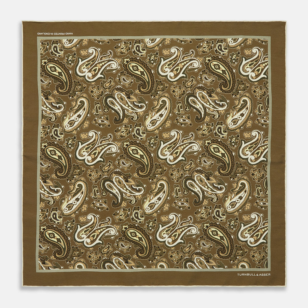 A green and lemon silk pocket square featuring a blossoming paisley pattern with a solid edge. “Turnbull & Asser” is inscribed in one corner; expertly crafted in England.