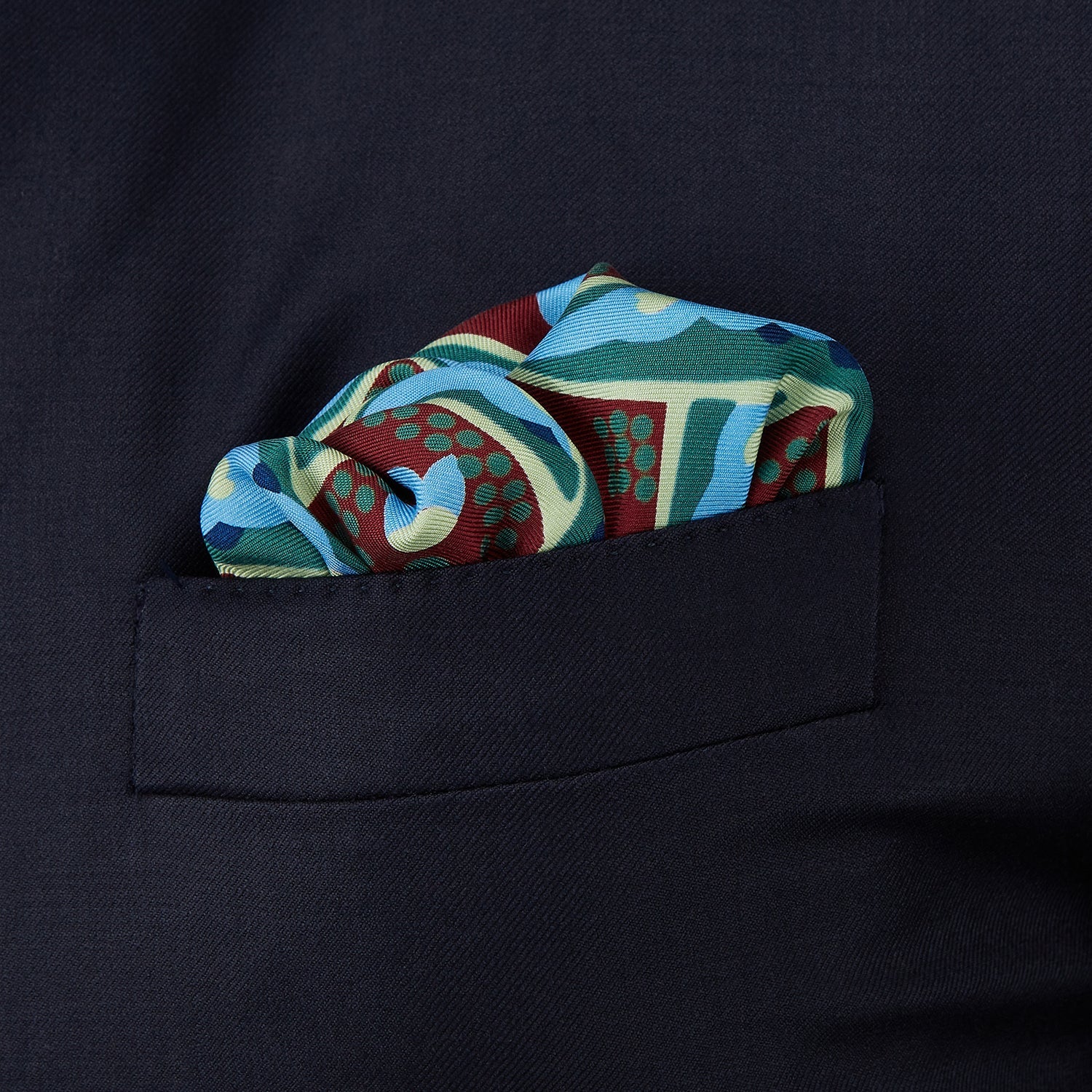 View 3 of product The Aqua and Burgundy Baroque Silk Pocket Square by Turnbull & Asser is crafted in England, featuring an intricate symmetrical pattern in teal, blue, red, and cream with ornate motifs framed by decorative borders.