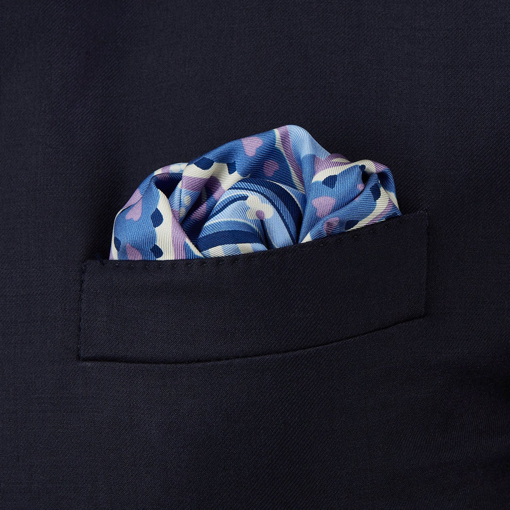 The Pale Blue and Lilac Baroque Silk Pocket Square by Turnbull & Asser features intricate geometric and floral patterns in blue, lilac, and white with a floral border and the brand name printed in one corner.