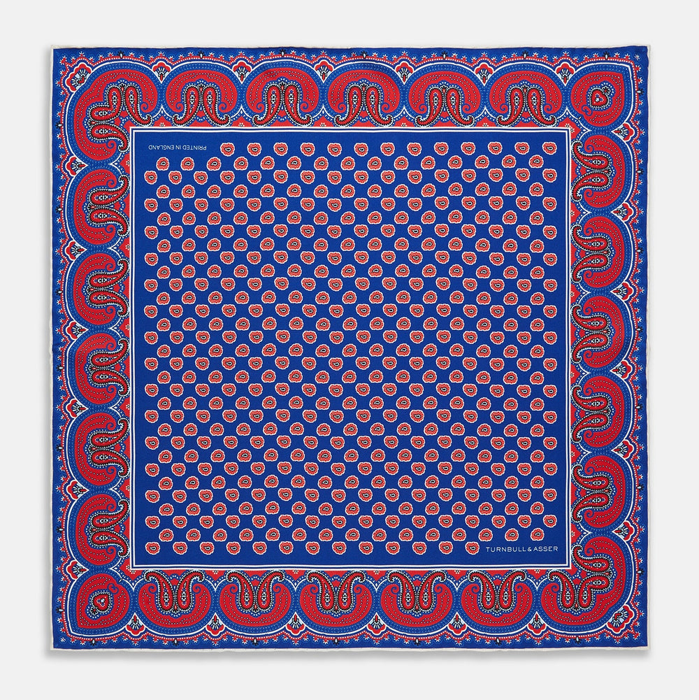 The Blue and Red Paisley Tiles Silk Pocket Square by Turnbull & Asser features a blue background, red and white paisley border, central repeating circular patterns, and “Turnbull & Asser” in one corner. Made in England.