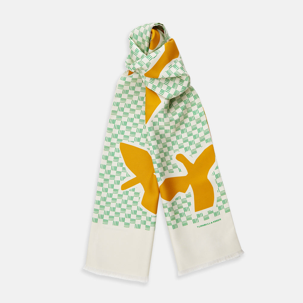 The Gold and Green Abstract Bird Silk Lawton Scarf by Turnbull & Asser features a white base with green checks, bold yellow Cubism-inspired bird motifs, and fringed edges, elegantly draped against a white background.