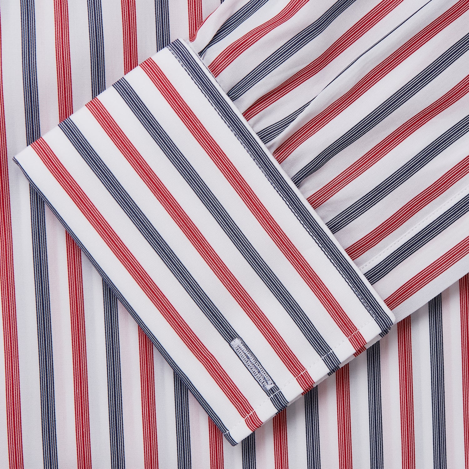 View 4 of product The Turnbull & Asser Red and Blue Stripe Cotton Regular Fit Whitby Shirt is a long-sleeve button-up featuring vibrant red and blue stripes on white, with a collar and buttoned cuffs, shown on a plain white surface.