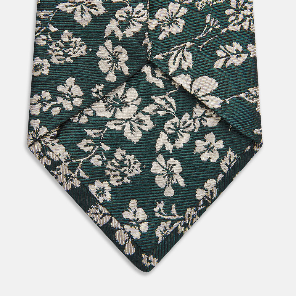The Turnbull & Asser Dark Green Floral Garden Silk Tie features an elegant white floral pattern on dark green silk, shown rolled against a plain white background.
