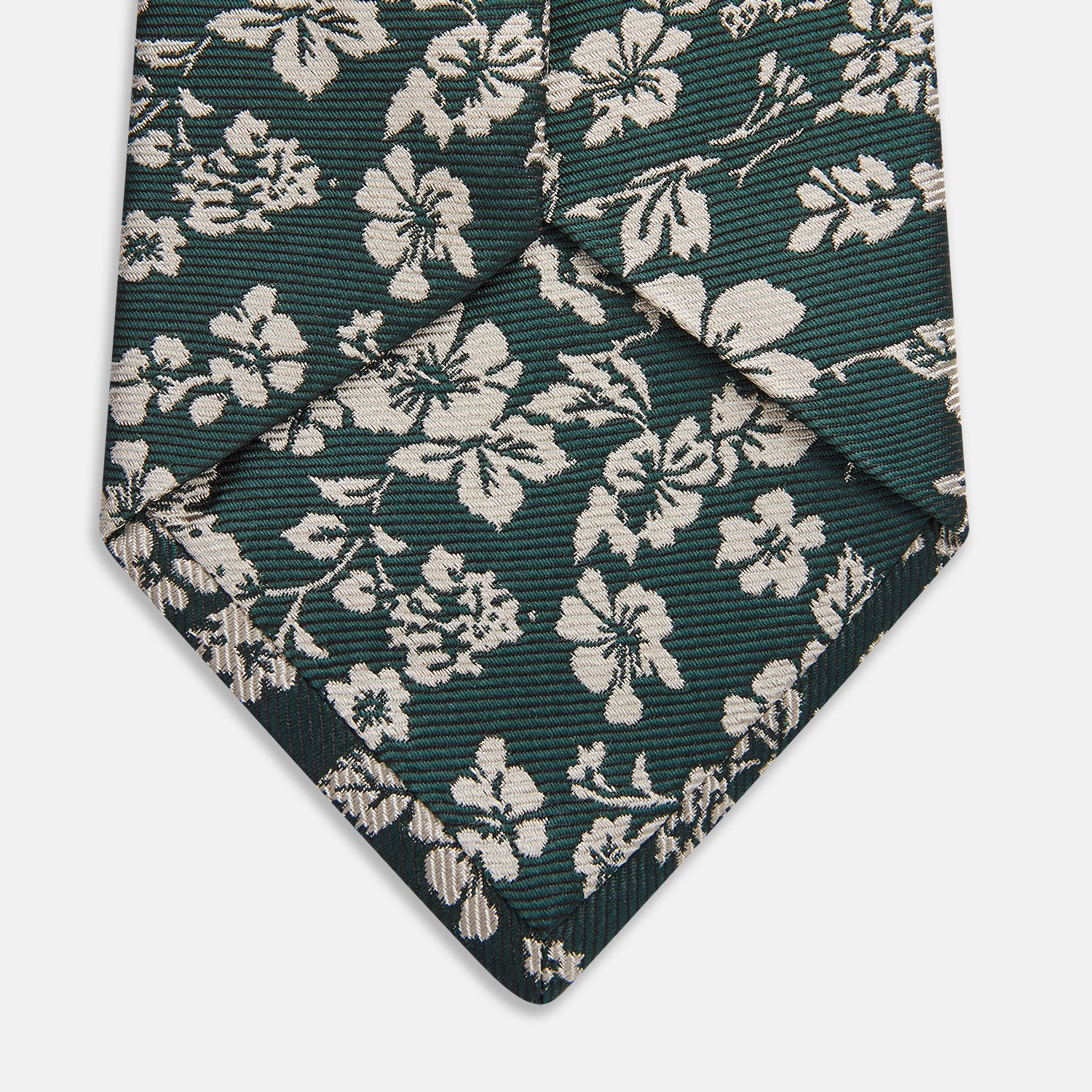 View 3 of product The Turnbull & Asser Dark Green Floral Garden Silk Tie features an elegant white floral pattern on dark green silk, shown rolled against a plain white background.