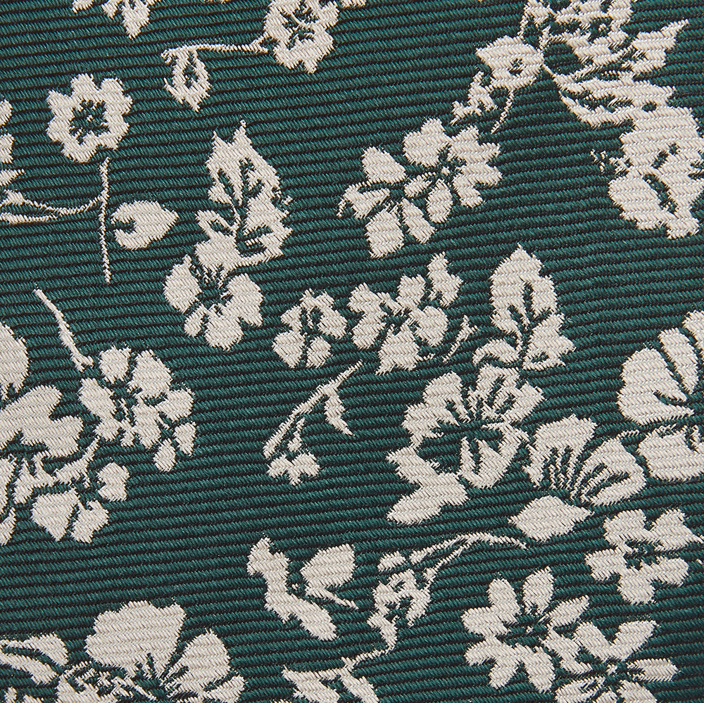 The Turnbull & Asser Dark Green Floral Garden Silk Tie features an elegant white floral pattern on dark green silk, shown rolled against a plain white background.