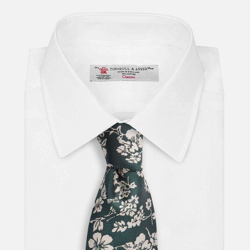 The Turnbull & Asser Dark Green Floral Garden Silk Tie features an elegant white floral pattern on dark green silk, shown rolled against a plain white background.