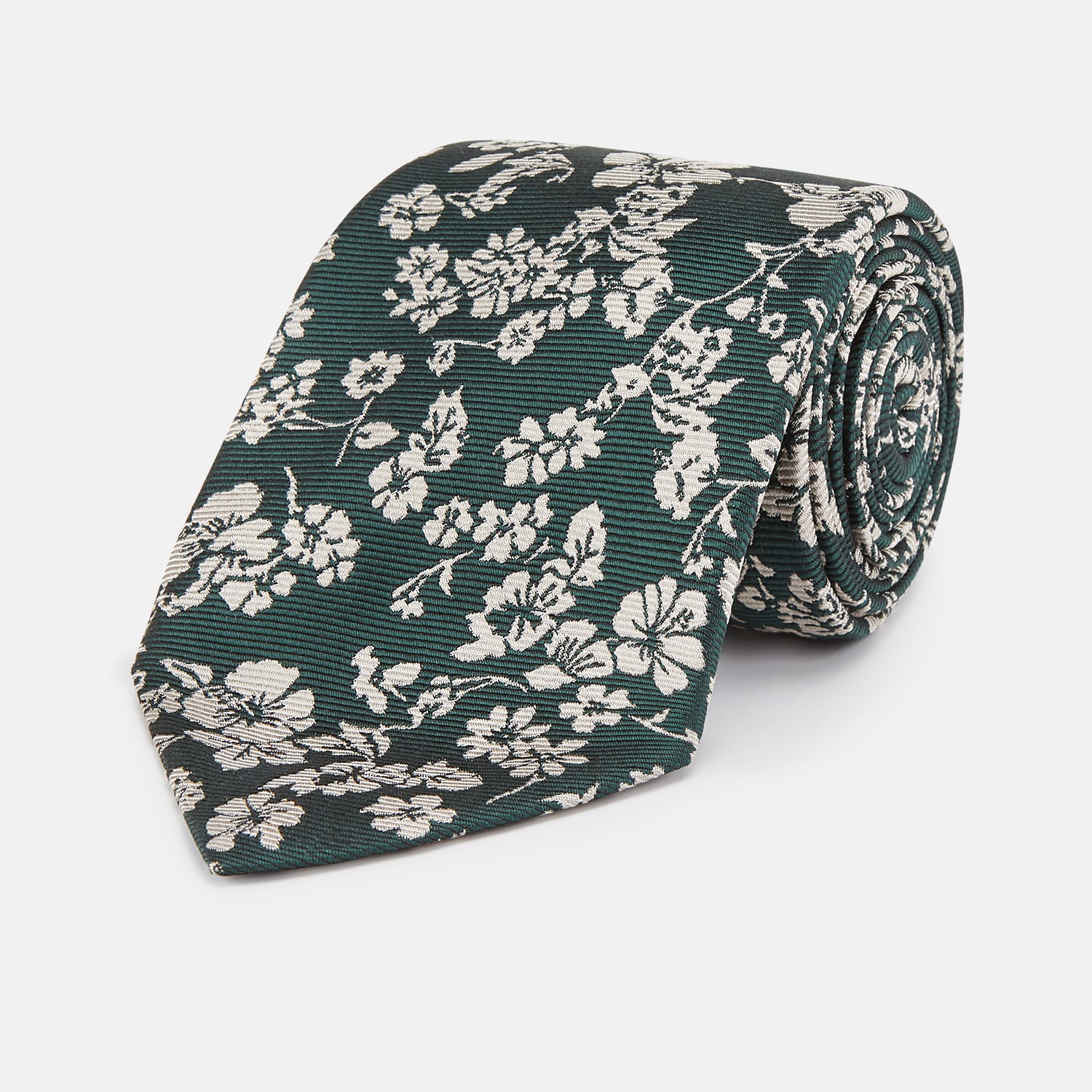 View 1 of product The Turnbull & Asser Dark Green Floral Garden Silk Tie features an elegant white floral pattern on dark green silk, shown rolled against a plain white background.