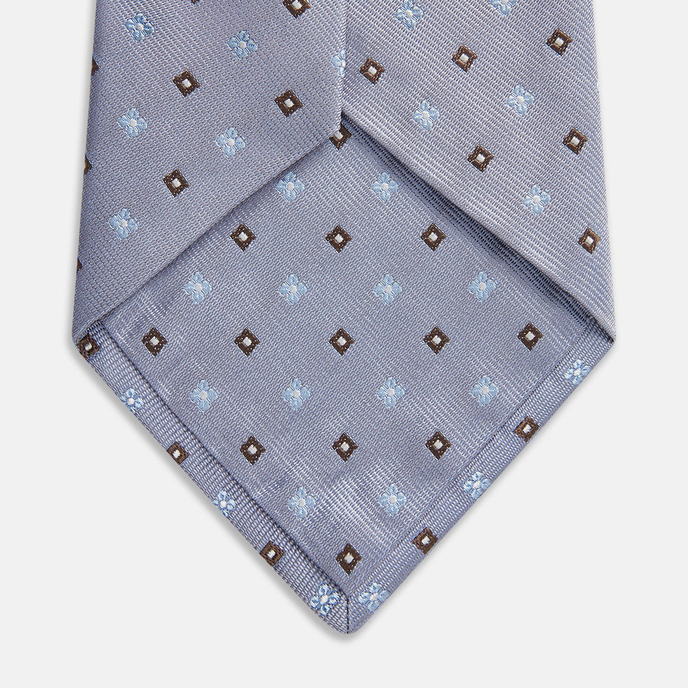 The Pale Blue Multi Floret Silk Tie by Turnbull & Asser features light purple silk with a pale blue floret pattern and small brown squares—perfect for pairing with a classic Turnbull & Asser shirt.