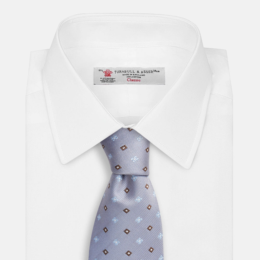 The Pale Blue Multi Floret Silk Tie by Turnbull & Asser features light purple silk with a pale blue floret pattern and small brown squares—perfect for pairing with a classic Turnbull & Asser shirt.