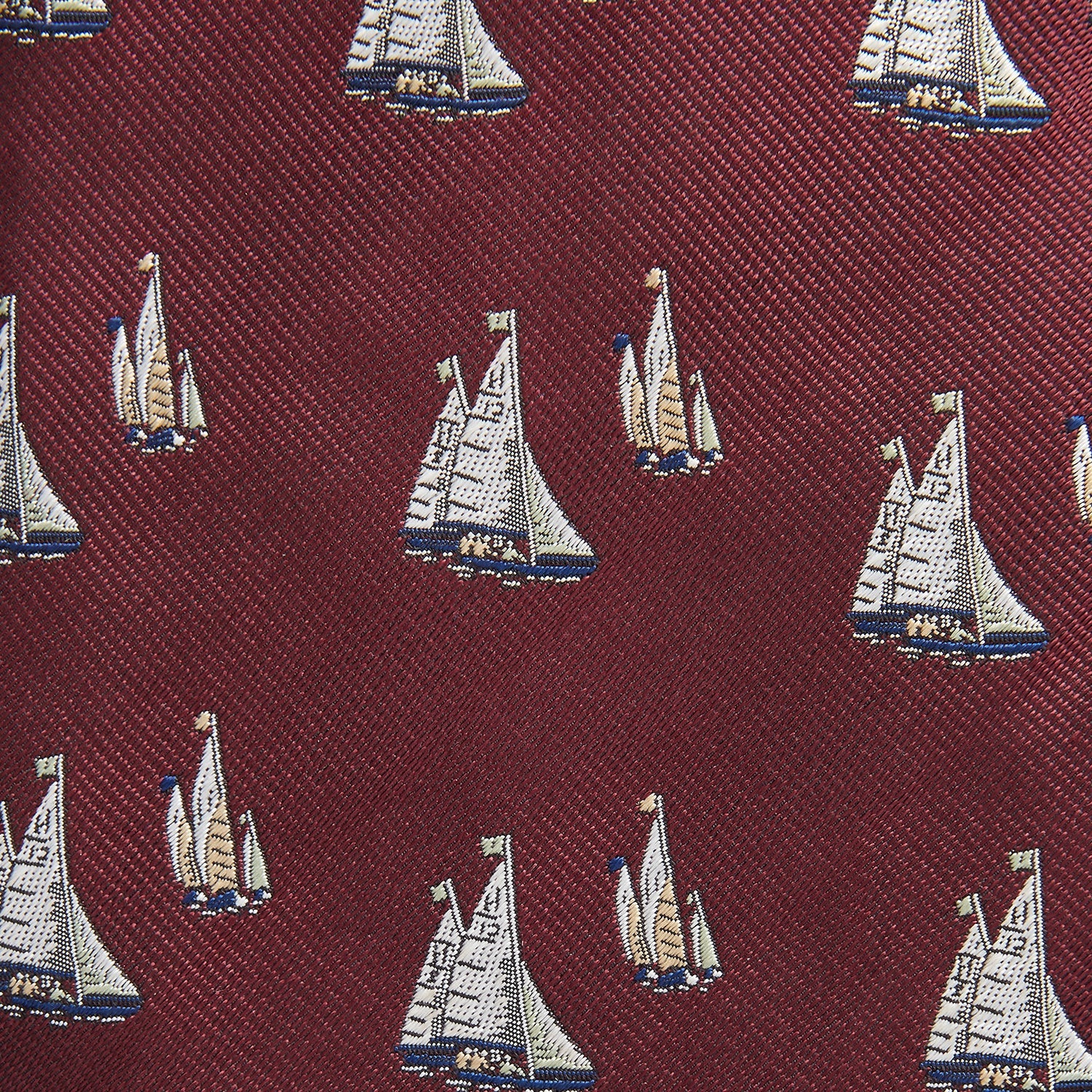 View 2 of product The Turnbull & Asser Burgundy Racing Yachts Silk Tie features a nautical sailboat pattern in white, blue, and brown on burgundy silk, shown rolled up against a plain white background.
