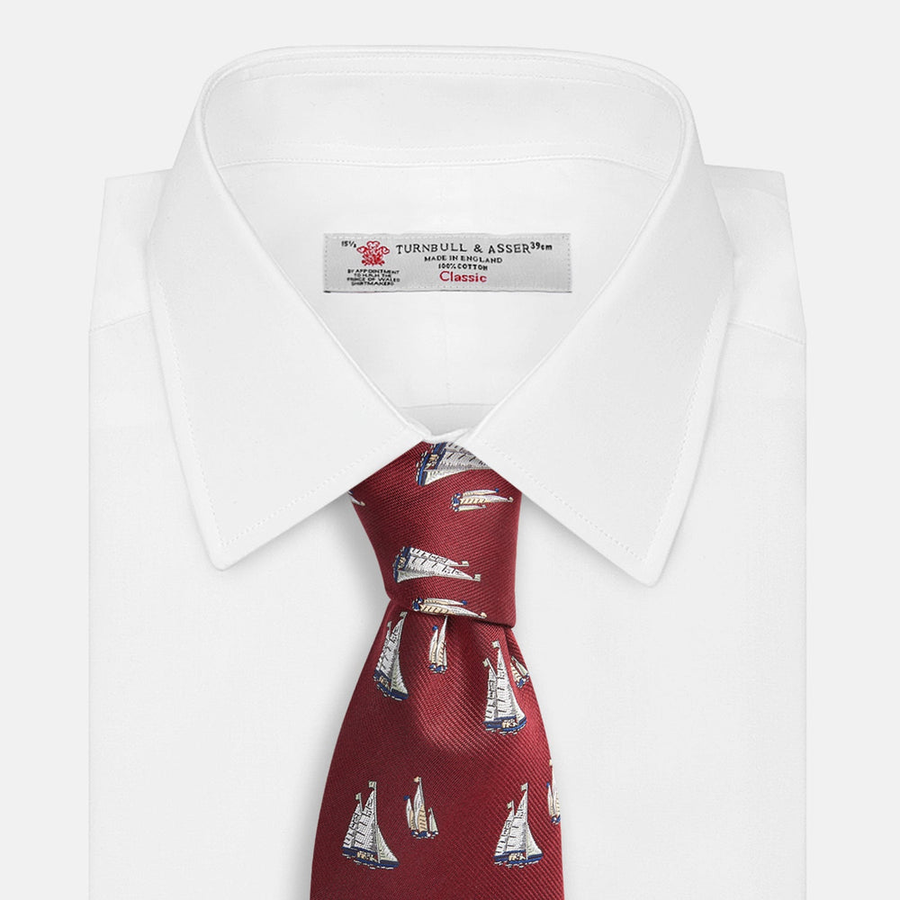 The Turnbull & Asser Burgundy Racing Yachts Silk Tie features a nautical sailboat pattern in white, blue, and brown on burgundy silk, shown rolled up against a plain white background.