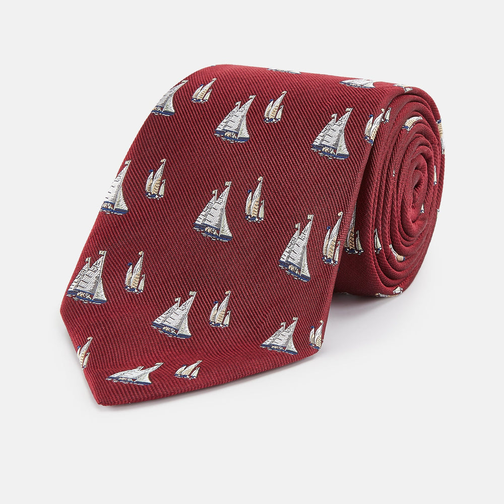 The Turnbull & Asser Burgundy Racing Yachts Silk Tie features a nautical sailboat pattern in white, blue, and brown on burgundy silk, shown rolled up against a plain white background.