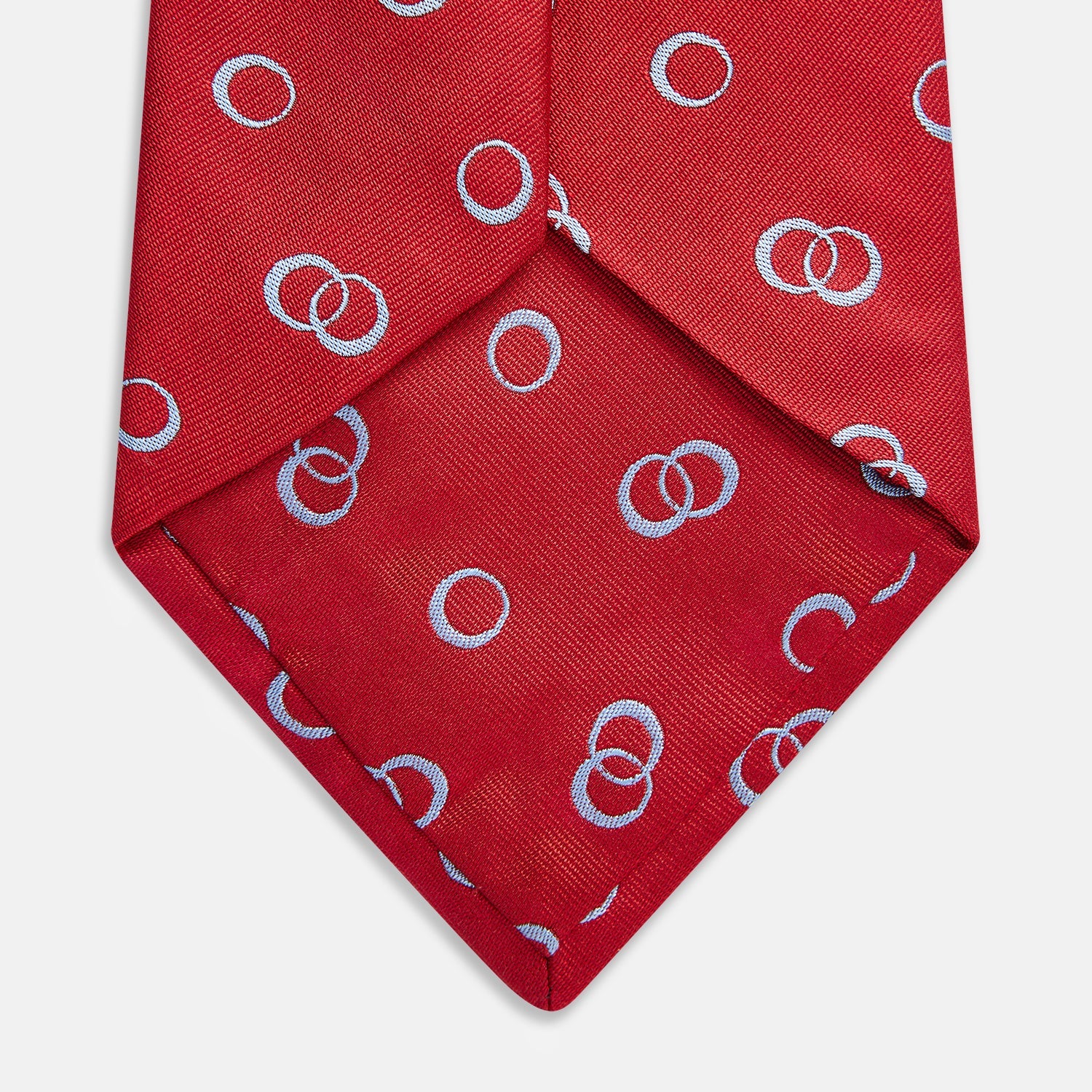 View 3 of product The Turnbull & Asser Red Geometric Rings Silk Tie, made in England, features a rolled-up design with small overlapping light blue circles on red silk and is displayed against a plain white background.