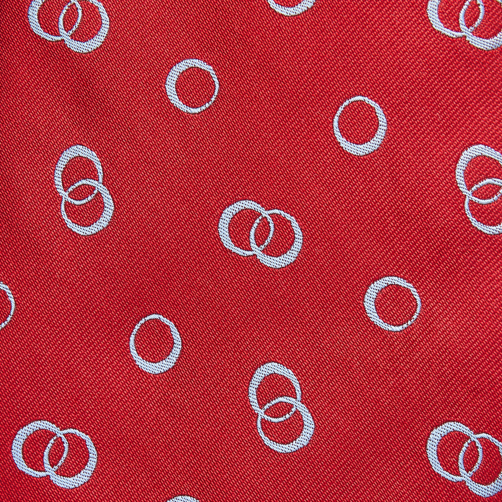 The Turnbull & Asser Red Geometric Rings Silk Tie, made in England, features a rolled-up design with small overlapping light blue circles on red silk and is displayed against a plain white background.