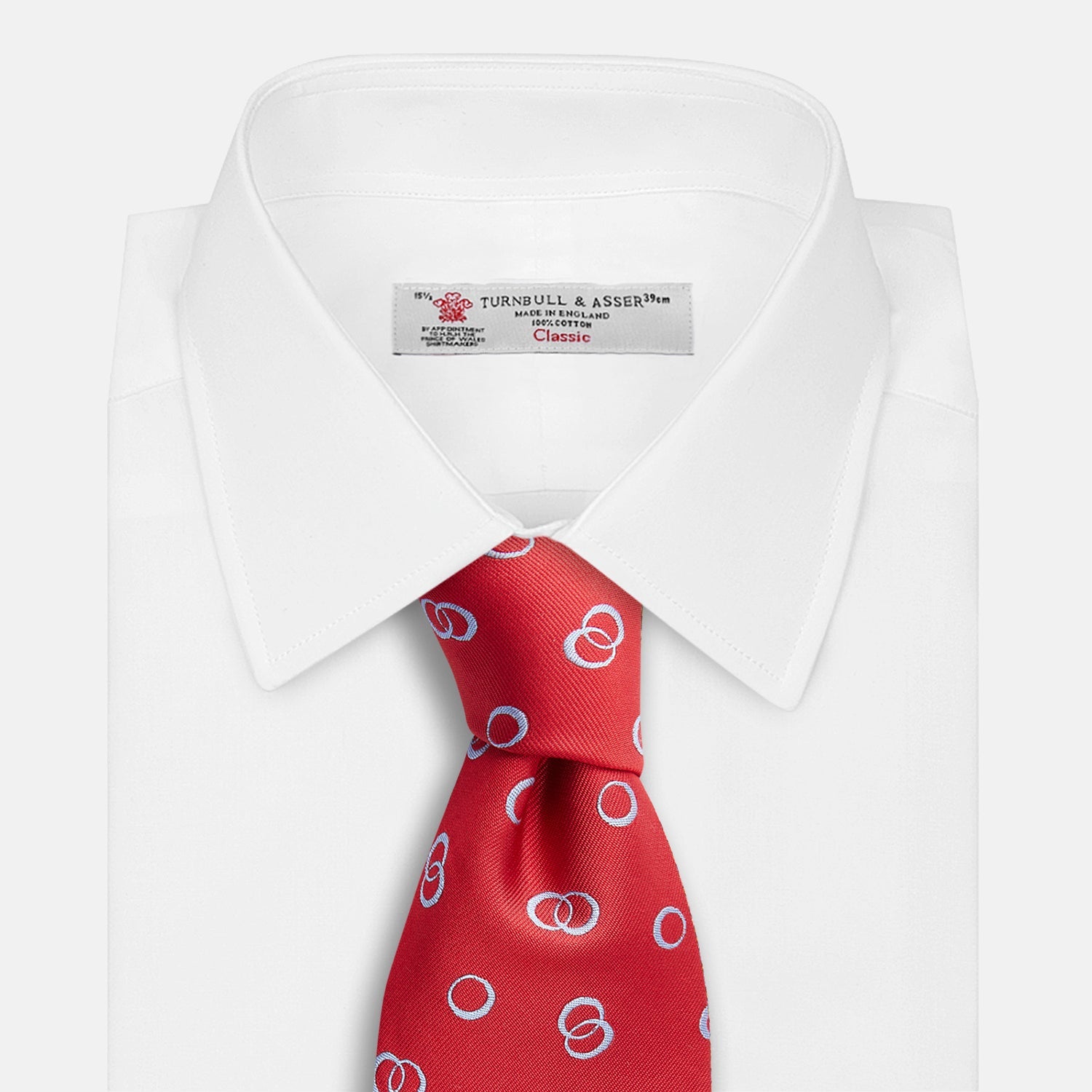 View 4 of product The Turnbull & Asser Red Geometric Rings Silk Tie, made in England, features a rolled-up design with small overlapping light blue circles on red silk and is displayed against a plain white background.