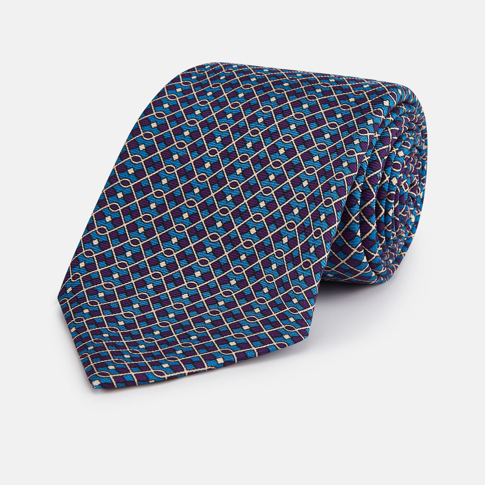 A rolled-up Pale Blue and Purple Art Deco Silk Tie by Turnbull & Asser, handmade in England, is displayed on a plain white background.