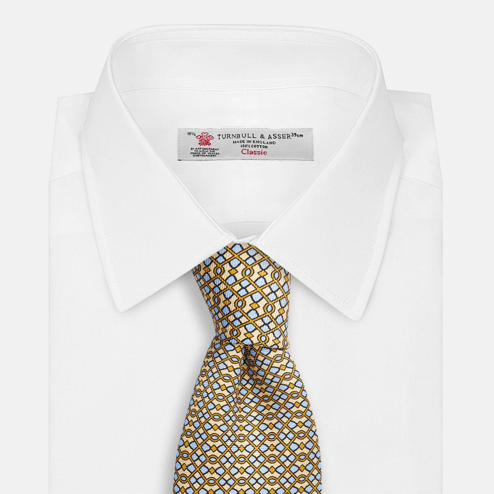 The Turnbull & Asser Yellow and Pale Blue Art Deco Silk Tie features interlocking yellow, blue, and black geometric shapes on white, adding a bold touch to any ensemble.