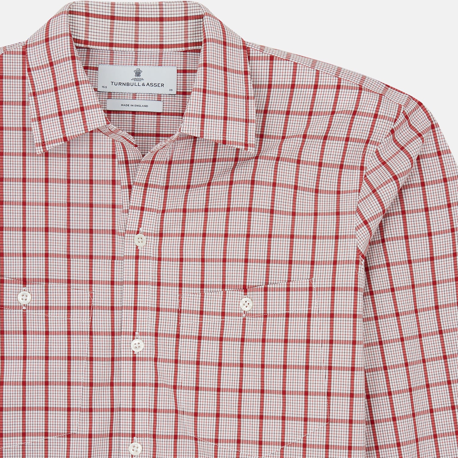 View 4 of product The Turnbull & Asser Red Graph Overlay Check Piccadilly Shirt is a cotton, long-sleeve button-up with a white base, red graph check pattern, collar, two chest flap pockets, and white buttons on the front and cuffs.