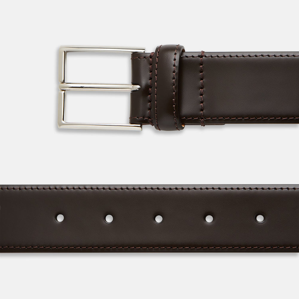 The Turnbull & Asser Dark Brown Nubuck Leather Evening Belt, featuring a silver rectangular buckle, is coiled neatly on a white background.