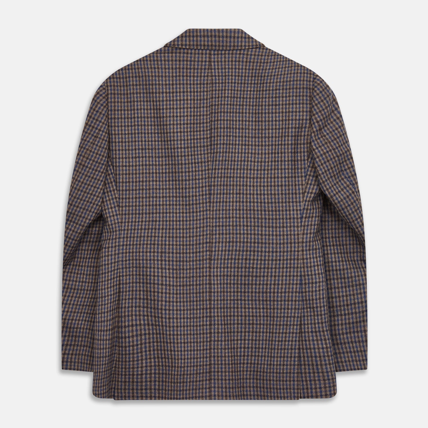 View 5 of product A man in glasses and a Turnbull & Asser Brown & Blue Check Merino Barrington Blazer, detailed with a colorful pocket square, stands thoughtfully indoors by patterned curtains, gazing out the window.