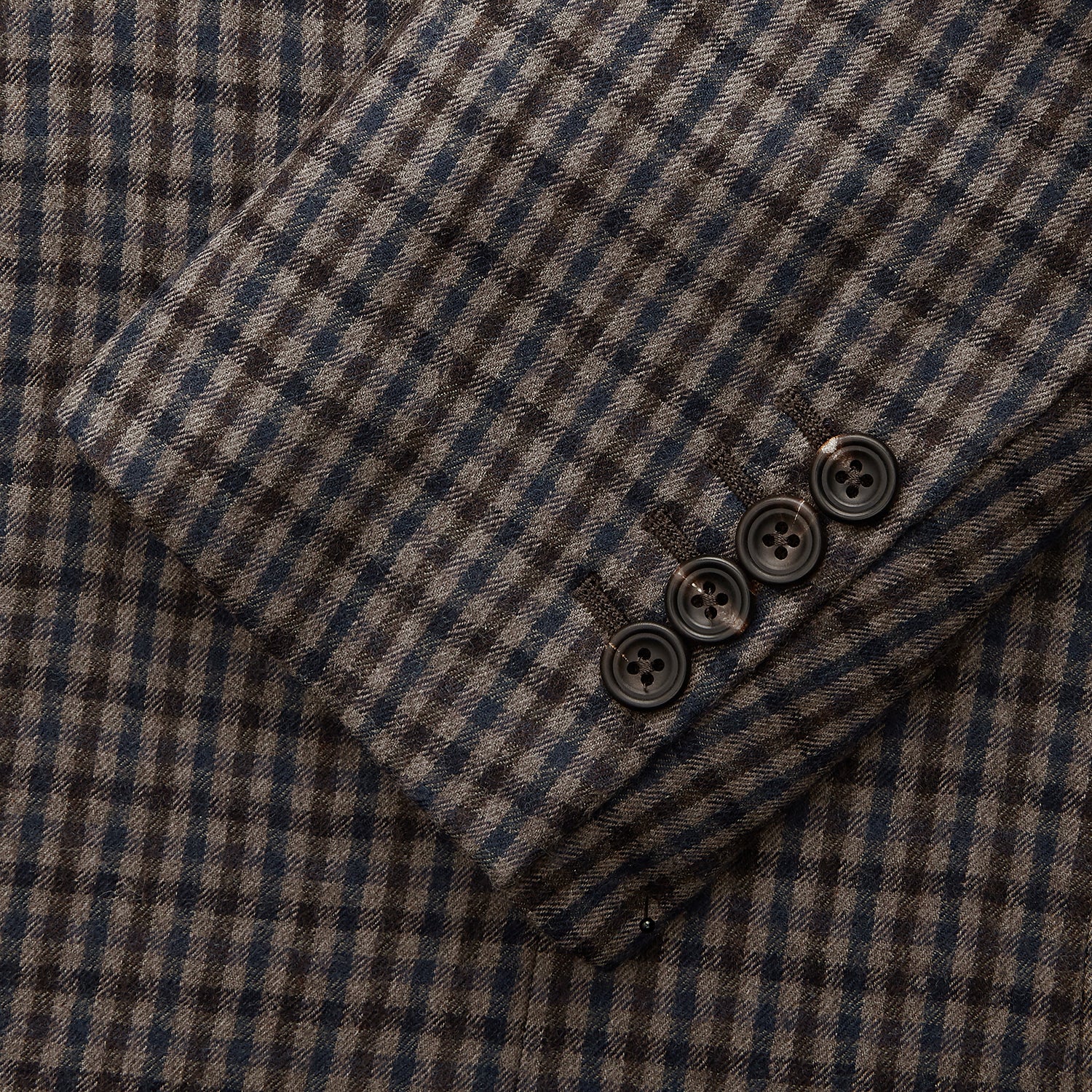View 4 of product A man in glasses and a Turnbull & Asser Brown & Blue Check Merino Barrington Blazer, detailed with a colorful pocket square, stands thoughtfully indoors by patterned curtains, gazing out the window.