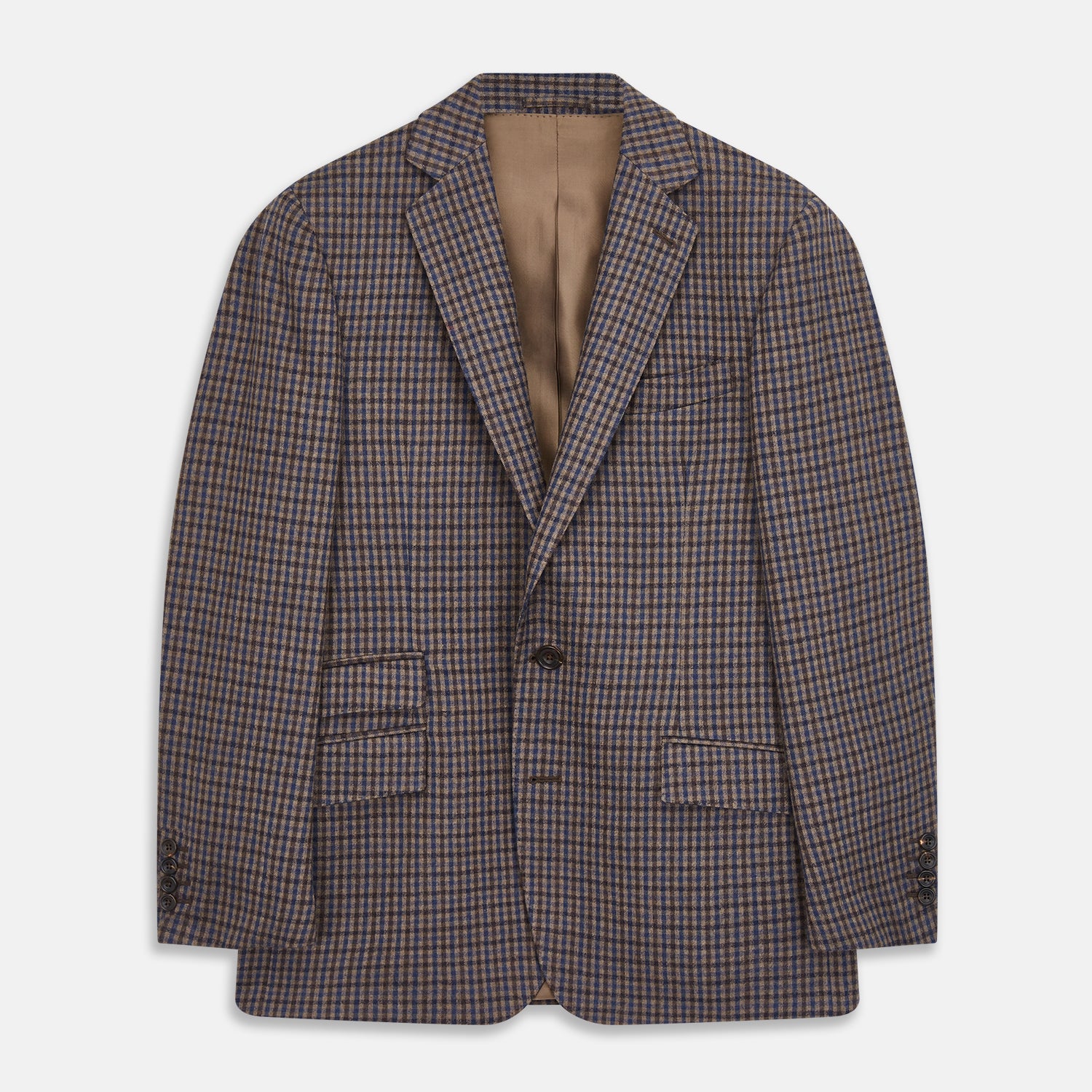 View 2 of product A man in glasses and a Turnbull & Asser Brown & Blue Check Merino Barrington Blazer, detailed with a colorful pocket square, stands thoughtfully indoors by patterned curtains, gazing out the window.
