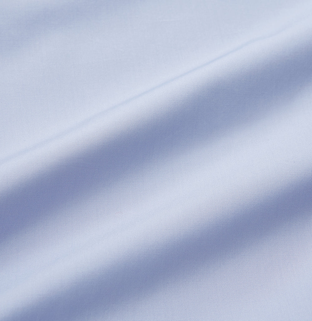 The Turnbull & Asser Blue Piped Sea Island Quality Cotton Nightshirt features light blue sea island cotton, a collared neckline with white piping, a front pocket, partial button placket, and a curved high-low hem for classic nightshirt style.