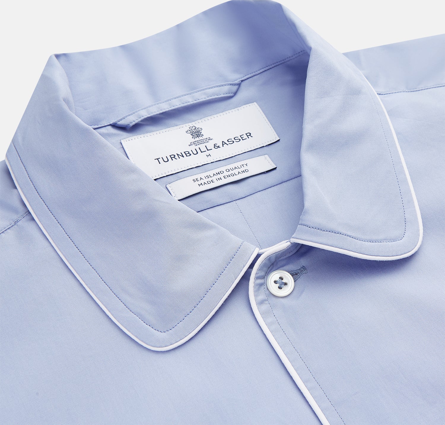 View 2 of product The Turnbull & Asser Blue Piped Sea Island Quality Cotton Nightshirt features light blue sea island cotton, a collared neckline with white piping, a front pocket, partial button placket, and a curved high-low hem for classic nightshirt style.