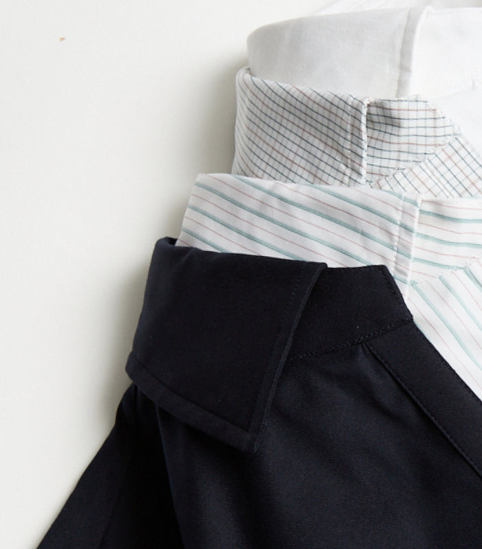 Three shirts stacked together, each with a distinct collar: a white dress shirt on top, a light blue striped shirt in the middle, and a dark-colored shirt on the bottom, all neatly layered against a plain background.