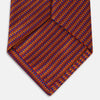 View 5 of product The Turnbull & Asser Die Another Day Stripe Silk Tie, as seen on James Bond, showcases a vibrant orange, red, and purple woven pattern, elegantly rolled and displayed against a white background.