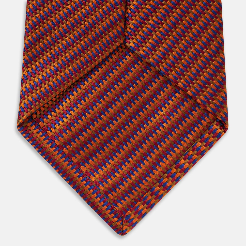 The Turnbull & Asser Die Another Day Stripe Silk Tie, as seen on James Bond, showcases a vibrant orange, red, and purple woven pattern, elegantly rolled and displayed against a white background.