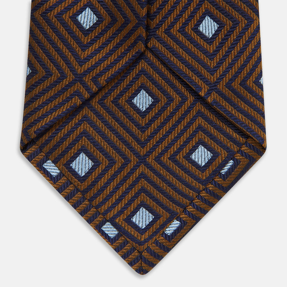 The Tomorrow Never Dies Square Silk Tie by Turnbull & Asser, as seen on James Bond, features a brown and blue geometric diamond pattern on a dark background—an ideal accessory for any Bond-inspired look. Displayed rolled on a plain white surface.