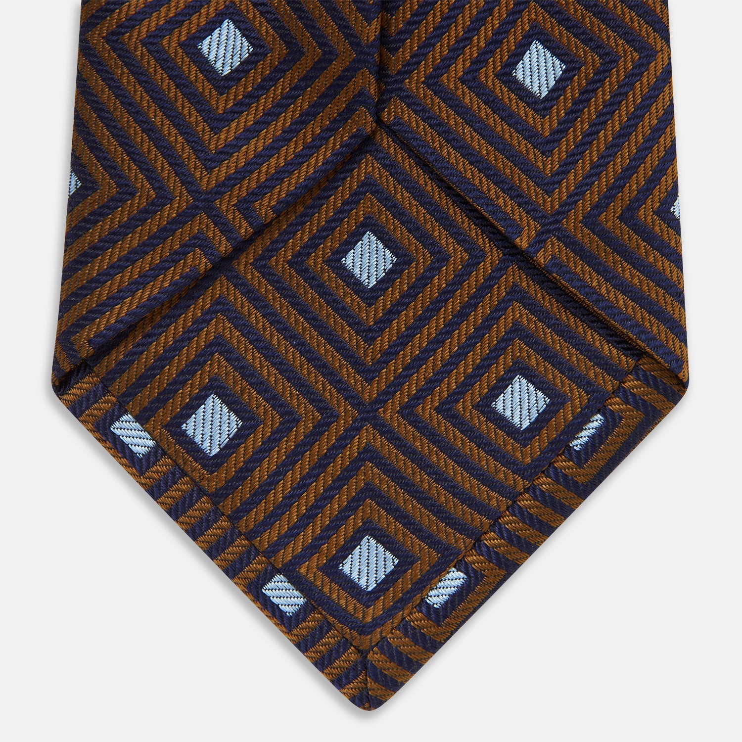 View 5 of product The Tomorrow Never Dies Square Silk Tie by Turnbull & Asser, as seen on James Bond, features a brown and blue geometric diamond pattern on a dark background—an ideal accessory for any Bond-inspired look. Displayed rolled on a plain white surface.