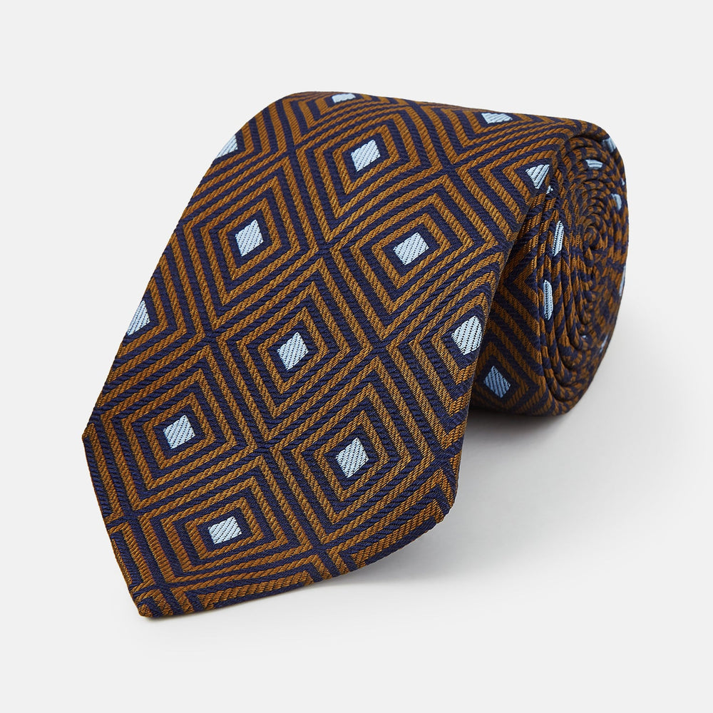 The Tomorrow Never Dies Square Silk Tie by Turnbull & Asser, as seen on James Bond, features a brown and blue geometric diamond pattern on a dark background—an ideal accessory for any Bond-inspired look. Displayed rolled on a plain white surface.