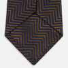 View 5 of product Turnbull & Asser's "The World Is Not Enough" Zig Zag Silk Tie, as seen on James Bond, features a bold navy blue and gold chevron design and is shown neatly rolled on a white background.