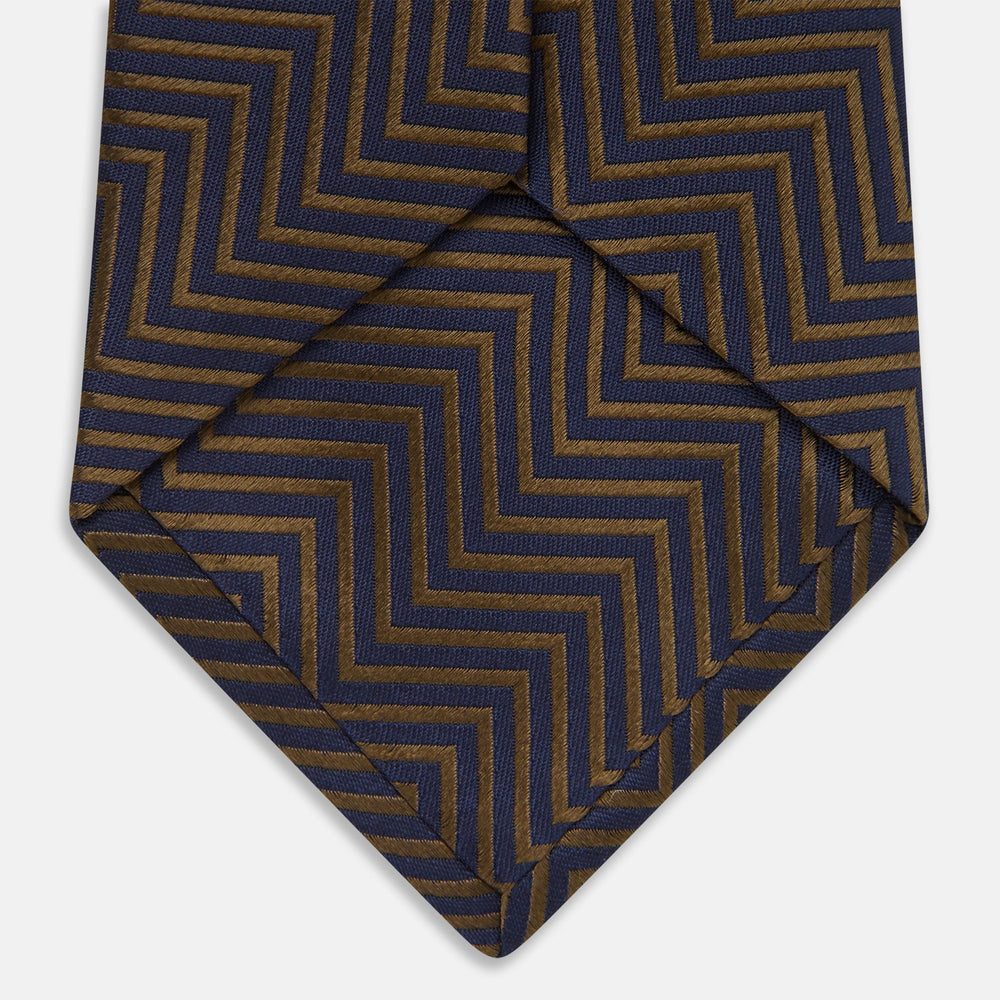 Turnbull & Asser's "The World Is Not Enough" Zig Zag Silk Tie, as seen on James Bond, features a bold navy blue and gold chevron design and is shown neatly rolled on a white background.