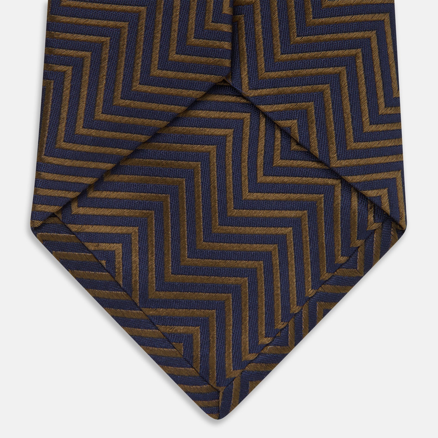 View 5 of product Turnbull & Asser's "The World Is Not Enough" Zig Zag Silk Tie, as seen on James Bond, features a bold navy blue and gold chevron design and is shown neatly rolled on a white background.