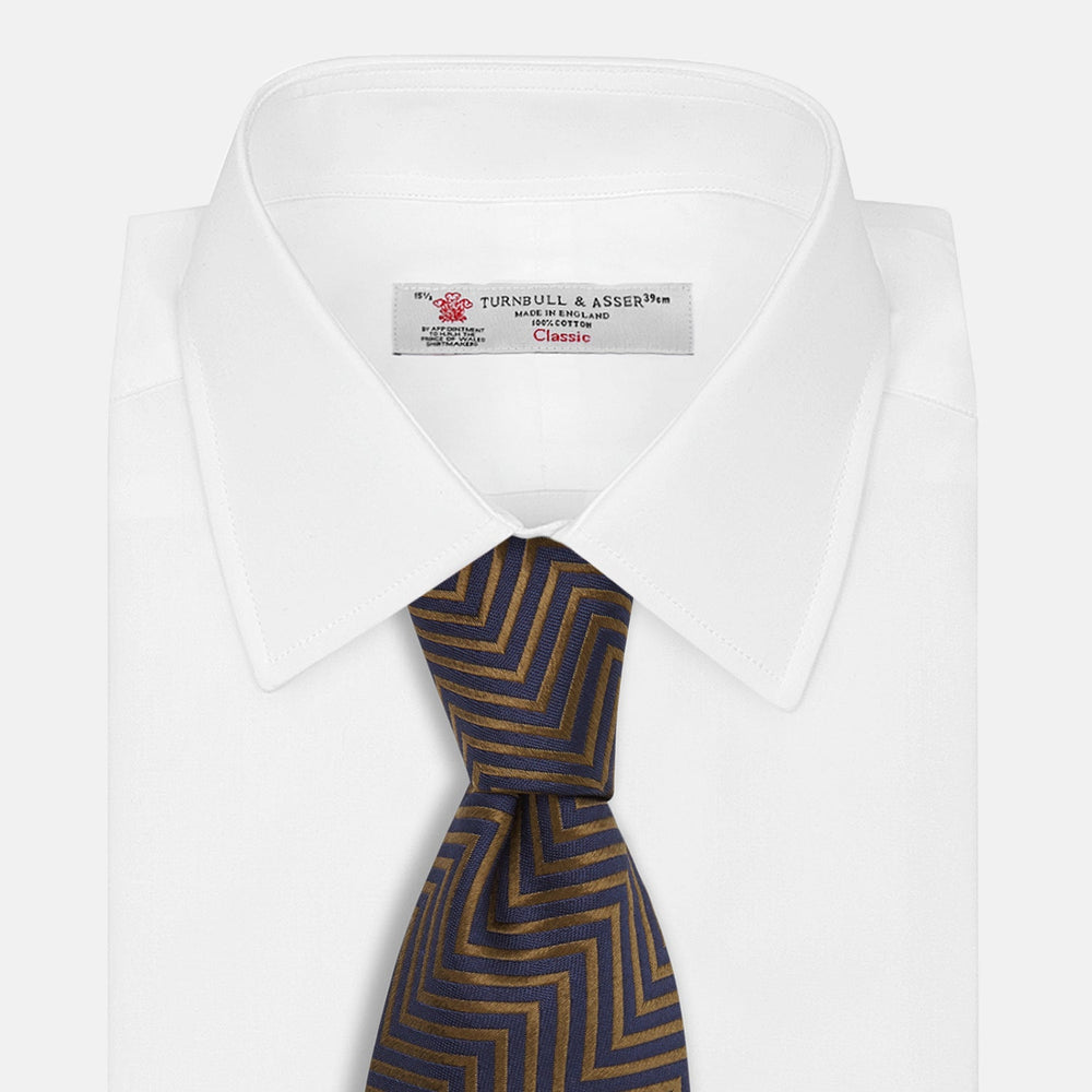 Turnbull & Asser's "The World Is Not Enough" Zig Zag Silk Tie, as seen on James Bond, features a bold navy blue and gold chevron design and is shown neatly rolled on a white background.