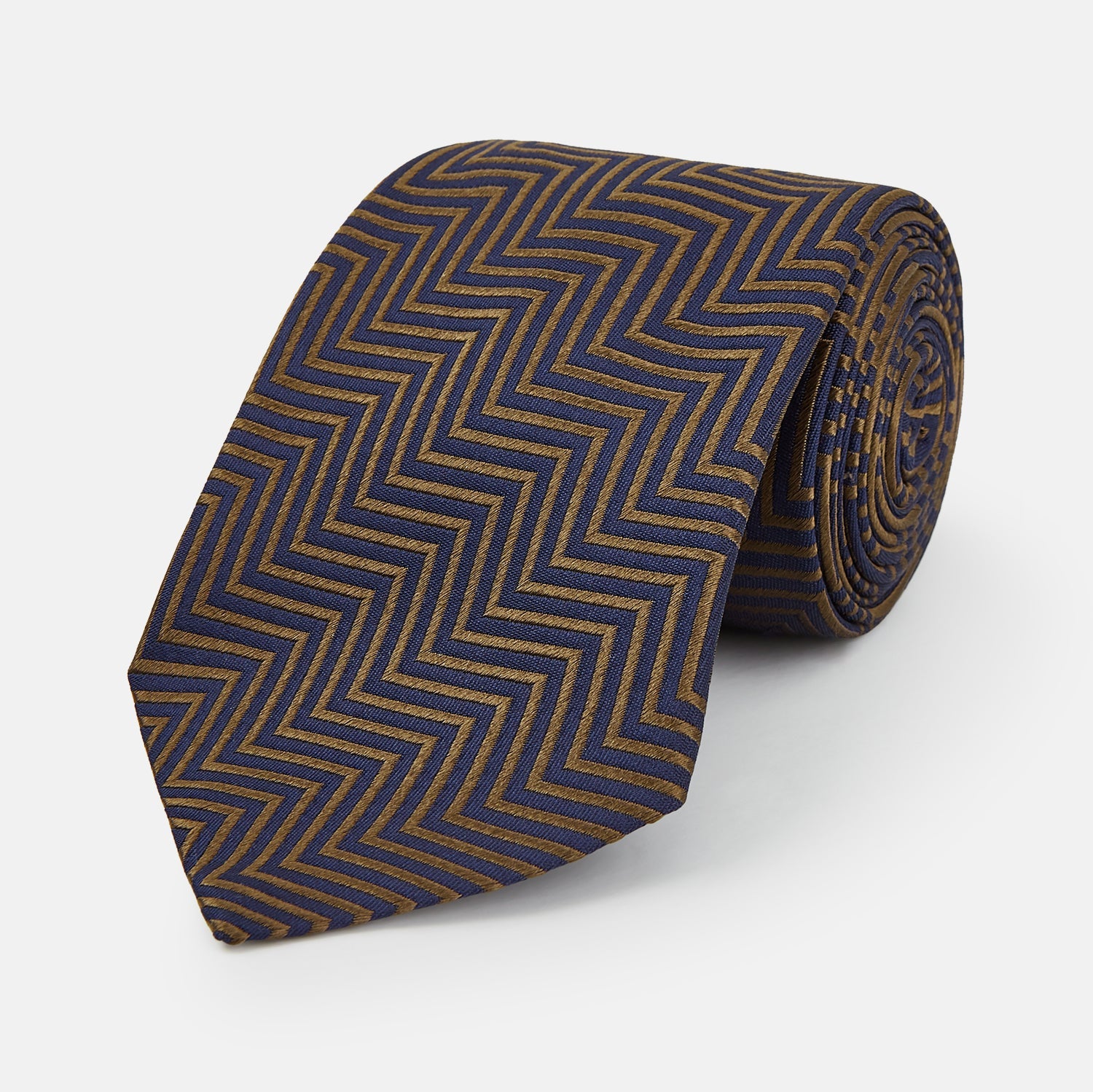 View 1 of product Turnbull & Asser's "The World Is Not Enough" Zig Zag Silk Tie, as seen on James Bond, features a bold navy blue and gold chevron design and is shown neatly rolled on a white background.