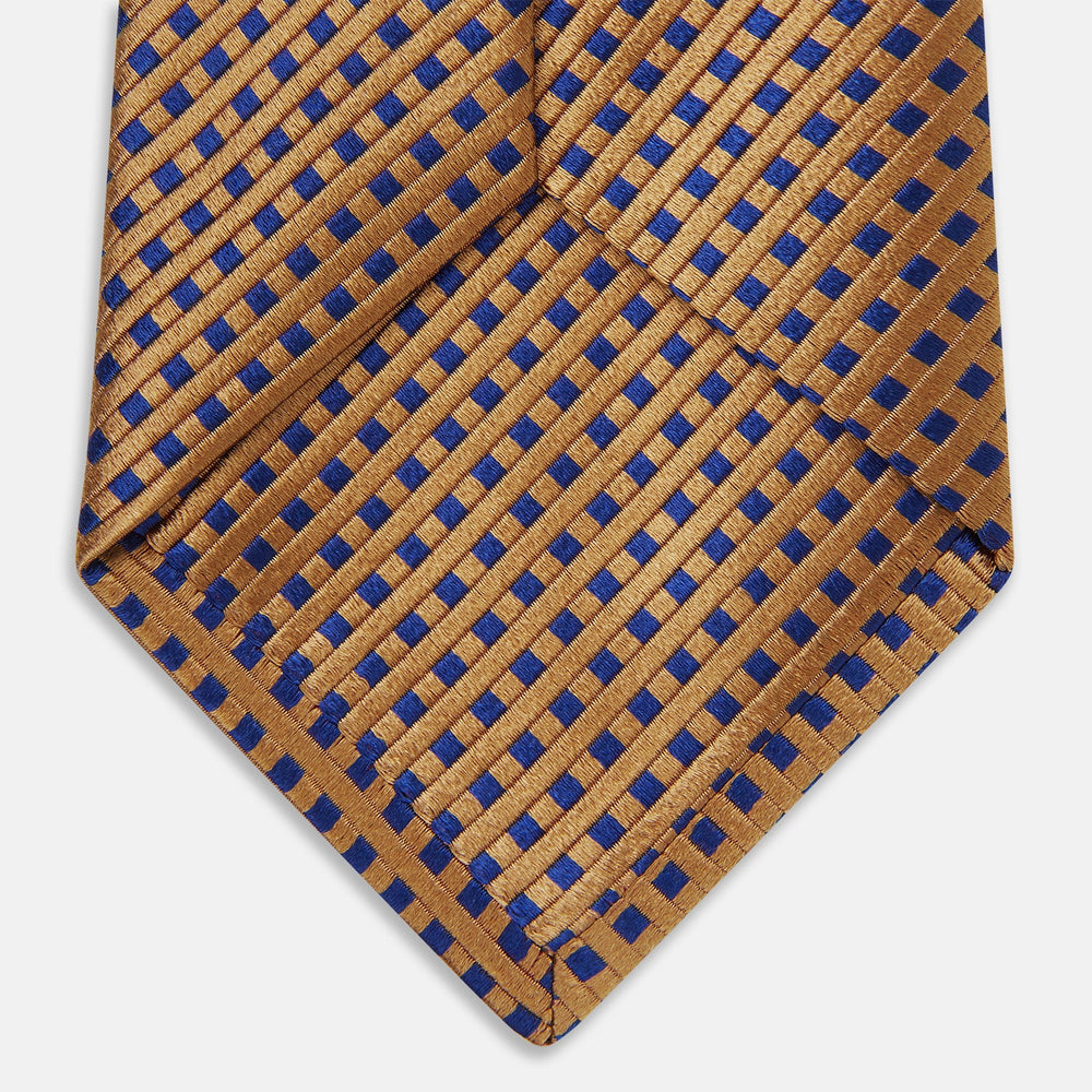 The Turnbull & Asser Tomorrow Never Dies Diamond Silk Tie, as seen on James Bond, features a gold and navy checkered pattern—an ideal gift for any Bond fan. Displayed rolled against a plain white background.