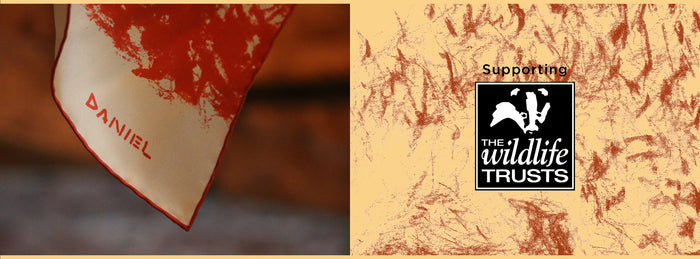 A close-up of a scarf with the name “Daniel” printed on it, alongside a banner reading “Supporting The Wildlife Trusts” with the charitys logo on a textured beige background.