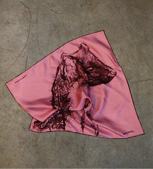 A pink silk scarf with a dark sketch of a hyenas head on it, lying on a gray concrete surface.