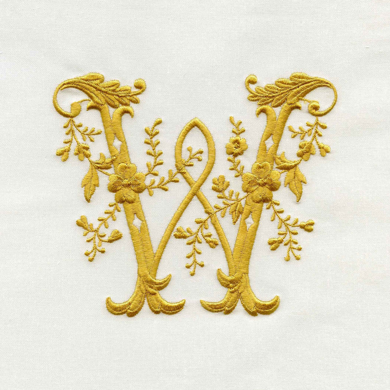 Turnbull & Asser's Embroidery features an ornate gold letter W on white fabric, adorned with intertwining floral and leaf patterns.