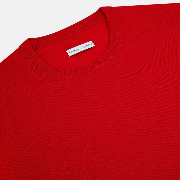 A close-up of a bright red crew neck sweater with a visible white label that reads Turnbull & Asser on the inside collar. The fabric appears smooth and neatly finished.