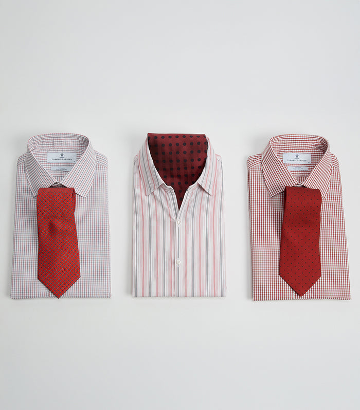 Three neatly folded dress shirts, each with a collar and paired with a red tie. The left and right shirts have checkered patterns with ties placed on top, while the center shirt is striped with an untied tie tucked inside.