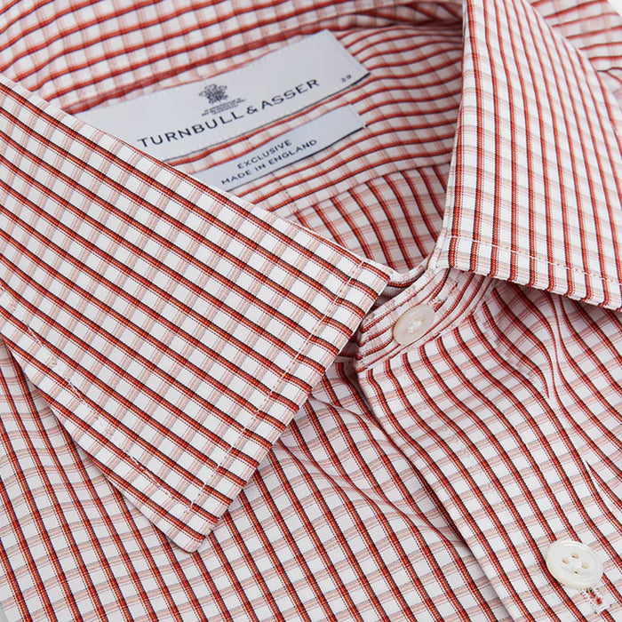 A close-up of a neatly folded Turnbull & Asser dress shirt with a white and red grid check pattern, showing the collar, buttons, and brand label inside the collar.