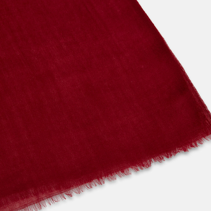 A close-up of a deep red fabric with a soft, slightly sheer texture and a frayed edge, displayed on a white background.