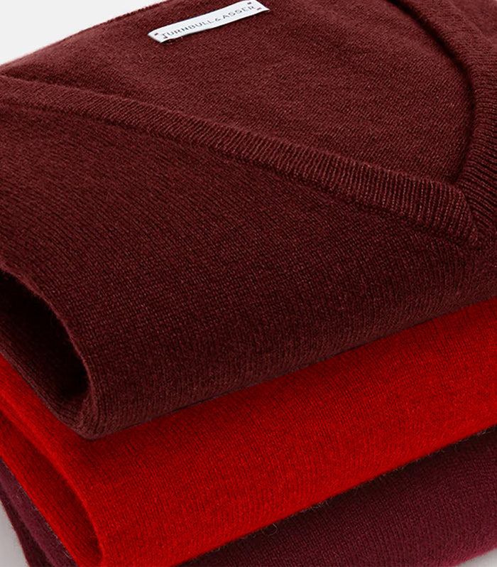 Two folded sweaters stacked on top of each other, one in deep maroon and the other in bright red. The top sweater features a label with text near the collar.